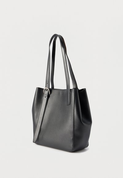 Μαύρη δερμάτινη τσάντα tote με δύο μακριά λουριά ώμου και ρυθμιζόμενο λουρί με πόρπη, εμφανιζόμενη πάνω σε απλό φωτεινό φόντο.