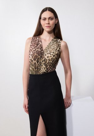 Majica bez rukava s leopard uzorkom, koja prelazi iz smeđe u zlatnu boju, u kombinaciji s uskom crnom suknjom s prednjim prorezom.