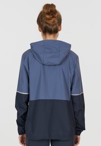 Giacca leggera con cappuccio in blu navy e blu, con dettagli riflettenti, vestibilità comoda e texture liscia, ideale per le attività all'aperto.