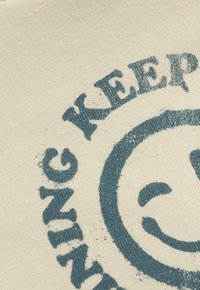 Nahaufnahme eines strukturierten Gewebes mit einem verblassten blauen Kreisdesign und teilweise lesbarem Text, der "WUNDER" liest.