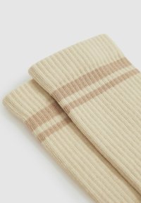 Beige, ribbede sokker med lysebrune striber foroven, der fremviser en blød tekstur og elastisk manchet-design.