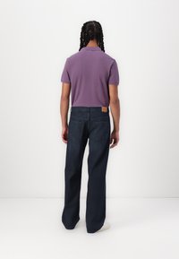 Purple polo shirt and dark blue wide-leg jeans, featuring a tan leather patch on the back waistband and visible back pockets.