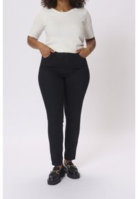 Un jean taille haute noir et un haut à manches courtes blanc, associés à des mocassins noirs avec des accents en doré.