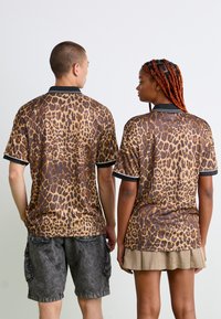 Du žmonės, atsisukę nugara, vilki derančius leopardų rašto trumpomis rankovėmis marškiniais; vienas yra juodų krovinių šortų, o kitas - kreminės spalvos sijono.