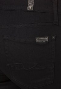 Jeans de mezclilla negra con un bolsillo trasero y costuras sutiles. La etiqueta dice "para toda la humanidad" y tiene el logo encima de la cinturilla.