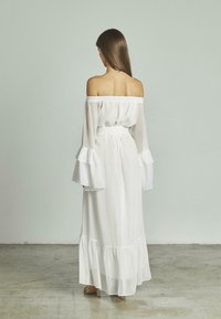 Schulterfreies weißes Kleid mit Rüschenärmel und gestuftem Saum, gefertigt aus leichtem Stoff mit einer glatten Textur.
