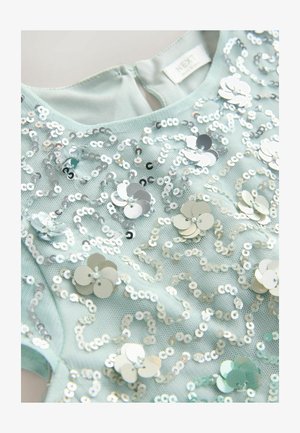 Mentolovo zelený top s textúrovaným prekrytím, zdobený striebornými flitrami v kvetinových a krúživých vzoroch, s uzáverom na zips na chrbte.