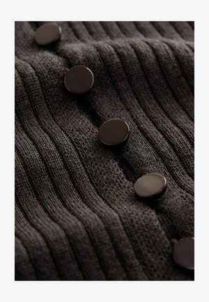 Bruin gebreid materiaal met verticale ribbelstructuur en ronde donkere knopen als detail. Knopen gelijkmatig verdeeld over het kledingstuk.