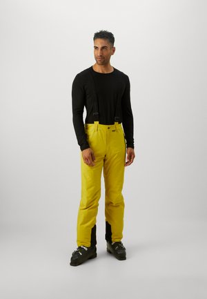 Pantaloni da sci gialli con bretelle nere regolabili, chiusura a bottone e dettagli neri alle caviglie, abbinati a una maglietta nera a maniche lunghe.