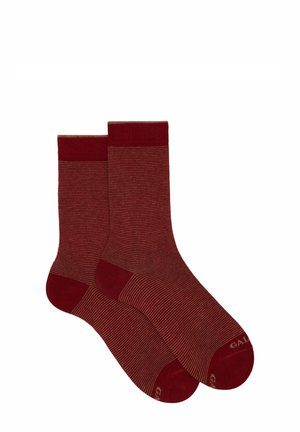 Calze a righe rosse con un bordo superiore a coste. Realizzate in un tessuto morbido, presentano una punta di un rosso più scuro. Sottili righe delicate lungo il corpo.