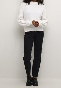 Witte gebreide trui met geribde zoom en gestructureerde mouwen, gecombineerd met zwarte broek met rechte pijpen en zwarte loafers. Eenvoudig ontwerp en neutrale kleuren.