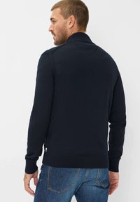 Marineblauwe gebreide cardigan met een geribde kraag en manchetten. Heeft een textuurdesign en een slim fit, gecombineerd met denim jeans.