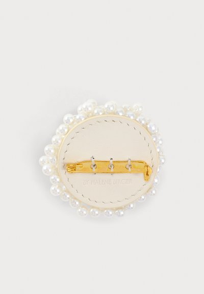 Broche ronde avec une épingle dorée à l'arrière, base en cuir blanc et bordure en petites perles blanches.
