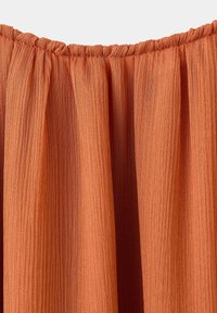 Jupe plissée en tissu orange rouille avec taille élastique froncée et matériau semi-transparent texturé.
