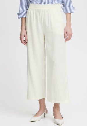 Leinen-Hosen mit weitem Bein in zartem Gelb und elastischem Bund. Kombiniert mit off-weißem, spitz zulaufendem Schuhwerk für einen Kontrast. Horizontale gestreifte Bluse sichtbar.