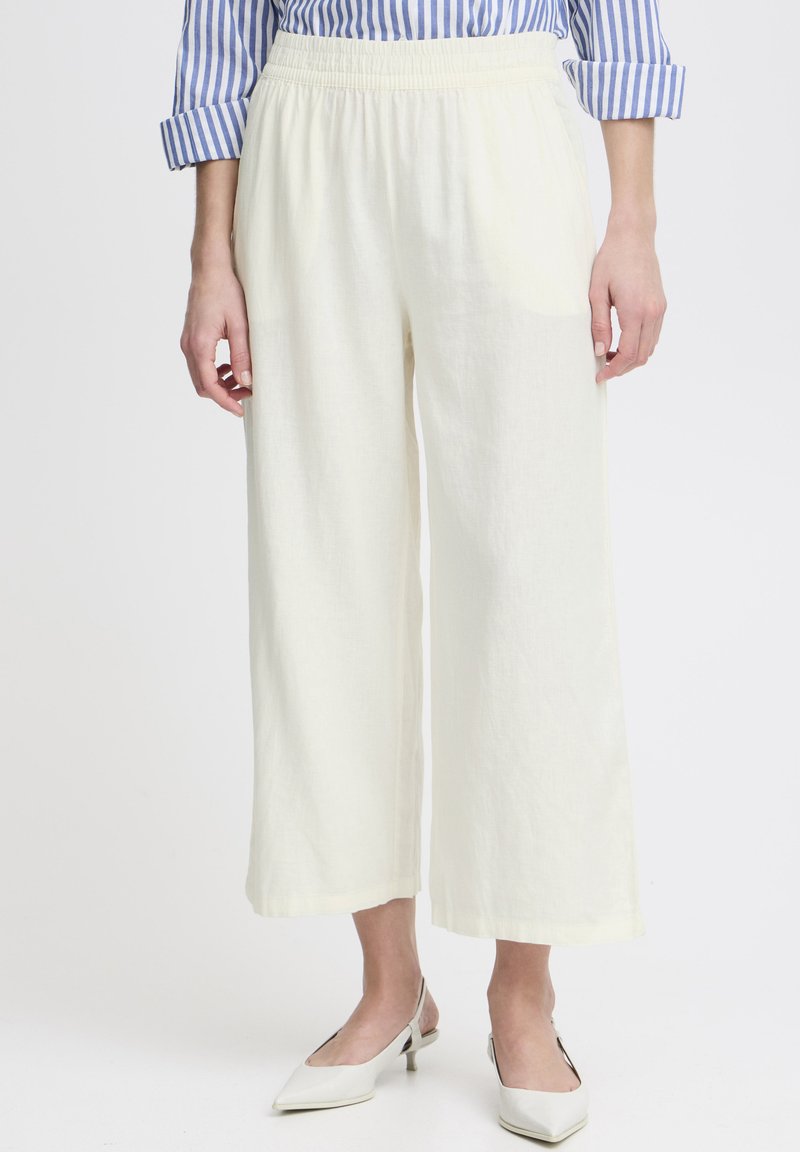 Puha sárga vászonnadrág széles lábakkal, rugalmas derékkal. Off-white, hegyes orrú ballerina cipővel párosítva, a kontraszt kedvéért. Látható vízszintes csíkos póló.