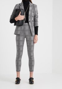 Blazer tailored grigio a motivo tartan con pantaloni slim-fit coordinati. Indossato sopra un dolcevita nero, accessorizzato con una pochette nera e mocassini.