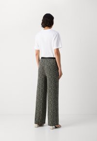 T-shirt blanc à manches courtes associé à un pantalon noir avec un motif abstrait texturé, coupe large et taille élastique.