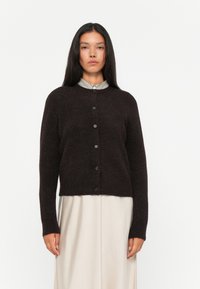 Cardigan marrone scuro realizzato in materiale morbido, con scollo tondo, maniche lunghe e sei bottoni centrali sul davanti.