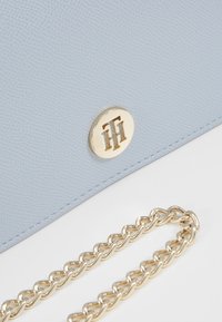 Jasnoniebieska torebka ze skóry z fakturą, z ozdobą w postaci złotego logo i złotym łańcuszkowym paskiem. Charakteryzuje się gładkim wykończeniem i kompaktowym designem.