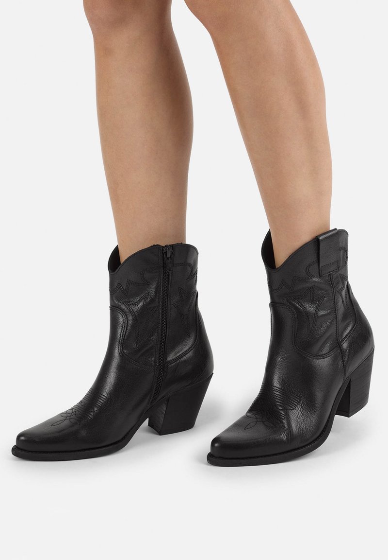 Botas de vaquero de cuero negro con puntas afiladas, un acabado texturizado, cremallera lateral y acentos de costura decorativa en la parte superior. Suela con tacón.