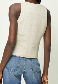 Beige mouwloze top van een gestructureerde stof, gecombineerd met high-waisted denim jeans met een klassieke snit en achterzakken.