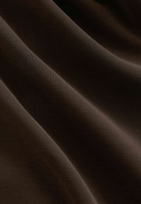 Tissu brun foncé, doux et lisse, avec de légers plis diagonaux créant des contrastes de lumière et d'ombre sur la surface.