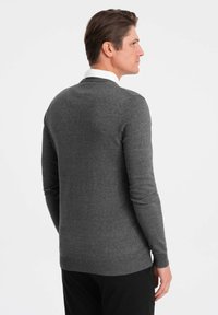 Pull en maille gris avec un col rond, coupe ajustée et manches longues. Présente des poignets et un ourlet côtelés, avec une texture lisse.