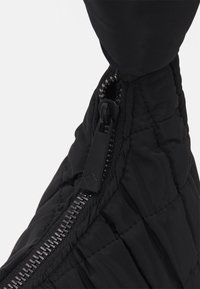 Bolso de plumas negro con textura acolchada, que presenta un cierre prominente y un tirador de ajuste. El material parece ligero y duradero.