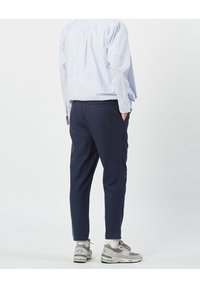 I pantaloni navy hanno un taglio slim, tasche laterali e un design semplice. Abbinati a una camicia a righe blu chiaro con bottoni e sneaker grigie.