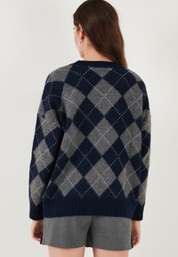 Navy and gray argyle-patterned sweater with a textured knit design, featuring a ribbed hem and visible stitching detail.