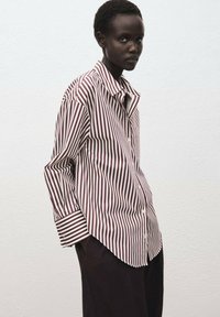 Camisa de botón con rayas verticales en burdeos y blanco, mangas largas con puños a rayas en contraste y un ajuste relajado.