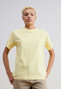 T-shirt en coton jaune à manches courtes et col rond, avec un logo subtil sur la poitrine et une coupe décontractée.