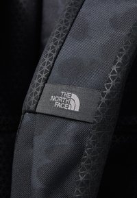Black fabric with a textured pattern features a gray label reading "THE NORTH FACE" and a logo, stitched neatly into the design.