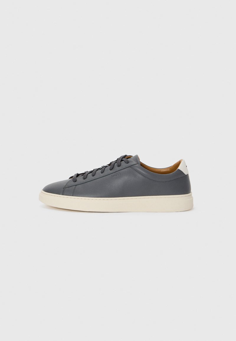 Grå skinnsneaker med rund tå, gummisåle, flate snører og lyse detaljer på hælen. Glatt tekstur og minimalistisk design.