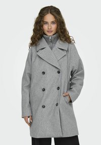 Cappotto grigio doppiopetto con grandi bottoni neri, colletto con rever e tasche laterali. Tessuto testurizzato e vestibilità comoda.