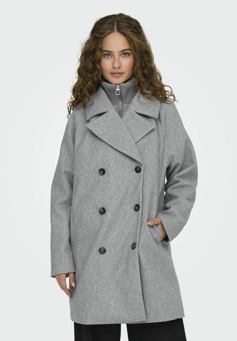 Cappotto grigio doppiopetto con grandi bottoni neri, colletto con rever e tasche laterali. Tessuto testurizzato e vestibilità comoda.