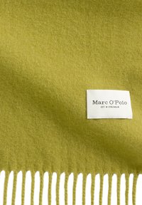 Zachte, olijfgroene wollen deken met een gladde textuur, voorzien van franjes aan één uiteinde en een wit label met het merk "Marc O’Polo".