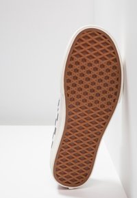 Sula med brunt gummimönster som har hexagonala och diamantformer, framför en vit bakgrund och vägghörn.