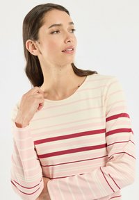 Haut à manches longues rayé avec des rayures pastel rose clair et crème alternées, agrémenté d'une large rayure bordeaux. Tissu doux avec une coupe décontractée.