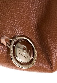 Borsa in pelle marrone con una targhetta logo circolare dorata, caratterizzata da un design a spirale e da una tracolla in pelle.
