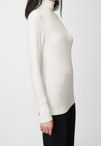Witte, lange mouwen turtleneck top met een aangesloten ontwerp en zachte textuur. Beschikt over een hoge kraag en naadloze manchetten. Gecombineerd met zwarte broek.