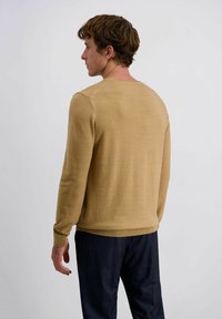 Hellbrauner Pullover mit Rundhalsausschnitt und langen Ärmeln sowie gerippten Bündchen, kombiniert mit dunkelkarierten Hosen; glatte Stricktextur.