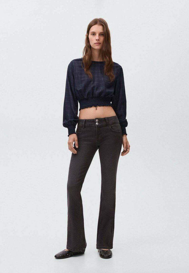 Marinblå kort topp med elastisk nederkant, med rutmönster; ihop med mörka utsvängda jeans med tvåknapps stängning och dekorerade svarta skor.