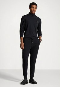 Svart turtleneck-genser og matchende joggebukser laget av mykt stoff, med snor i midjen og brodert logo.
