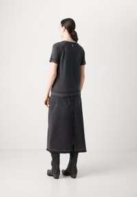 Top corto nero a maniche corte con scollatura tonda, abbinato a una lunga gonna di denim nera con spacco laterale e cuciture decorative. Stivali neri con tacco.