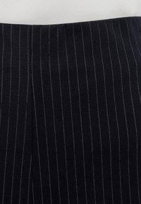 Mustast kangast vertikaalsete valgete triipudega, sileda tekstuuriga ja hoolikalt lõigatud disainiga. Ilma nähtavate kinnituste või kaunistusteta.