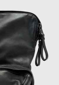 Černá kožená taška s hladkým povrchem, zipovým uzávěrem a štíhlým designem. Obsahuje kožený úchyt pro snadný přístup.