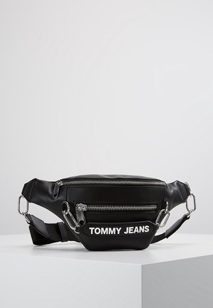 Czarna nerka Tommy Jeans z dwoma zamykanymi na zamek kieszeniami i regulowanym paskiem, umieszczona na białej powierzchni na jednolitym tle.