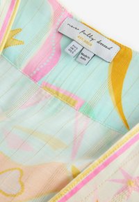 Farebná tkanina odevu s abstraktnými pastelovými vzormi a detailmi zo zlatého vlákna, obsahujúca veľkostné štítky a označenie značky s nápisom "never fully dressed."